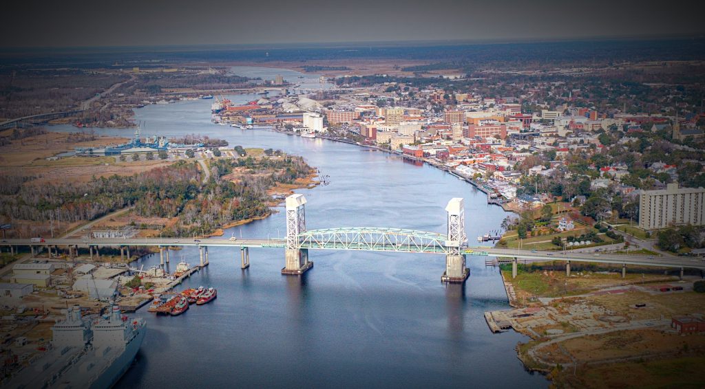 Aerial view of a river with a bridge, surrounded by a cityscape and greenery, in Wilmington, North Carolina.